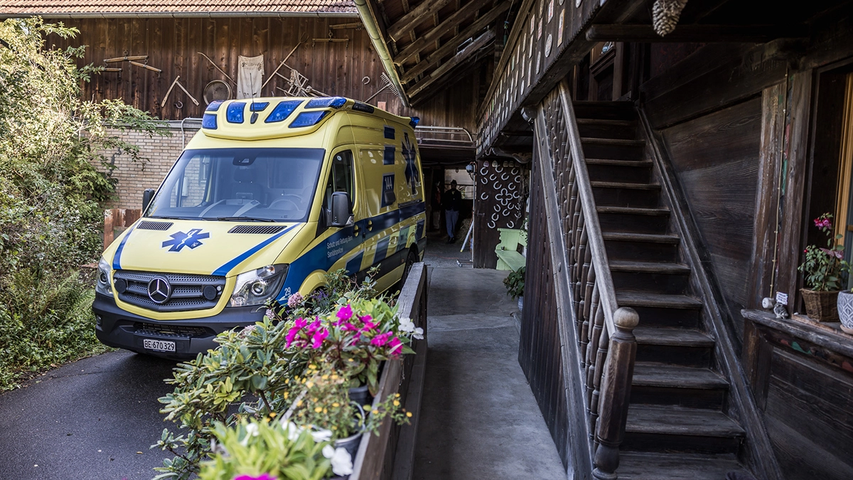 Une ambulance des services de secours est stationnée devant une ferme traditionnelle lors d'une intervention pour fournir une assistance médicale sur place.