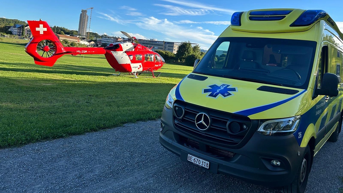 Ambulance et hélicoptère de la Rega lors d'une intervention d'urgence conjointe dans un champ, collaboration entre les secours aériens et les services de secours en Suisse.